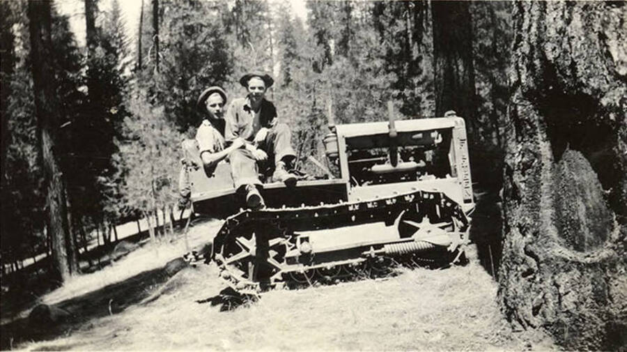 Two CCC men sitting atop a bulldozer in the woods. Writing under the photo reads: ''Tex', I  and the 'Pussy''.