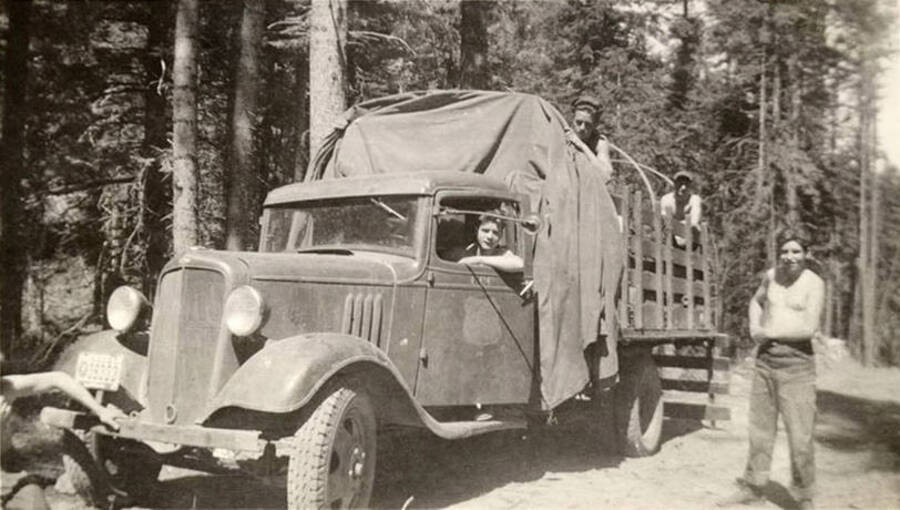 Four CCC men pose in and around a truck. Letters on the truck door read: 'CCC' But there is a visible spot on the door in the shape of a crest, likely where the Forest Service Emblem used to be displayed. Writing under the photo reads: 'Taking a Sun-bath'.