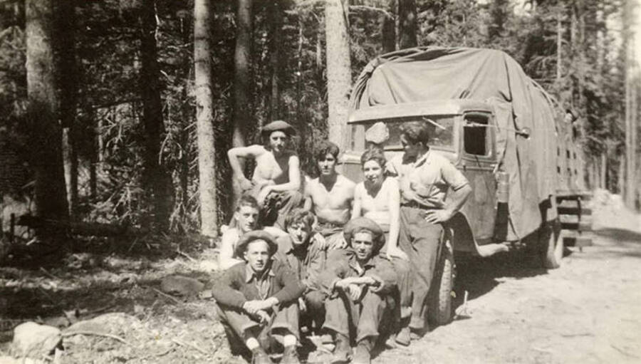 Eight CCC men pose in front of a truck in the middle of the woods. Writing under the photo reads: 'All 'Rookies''.
