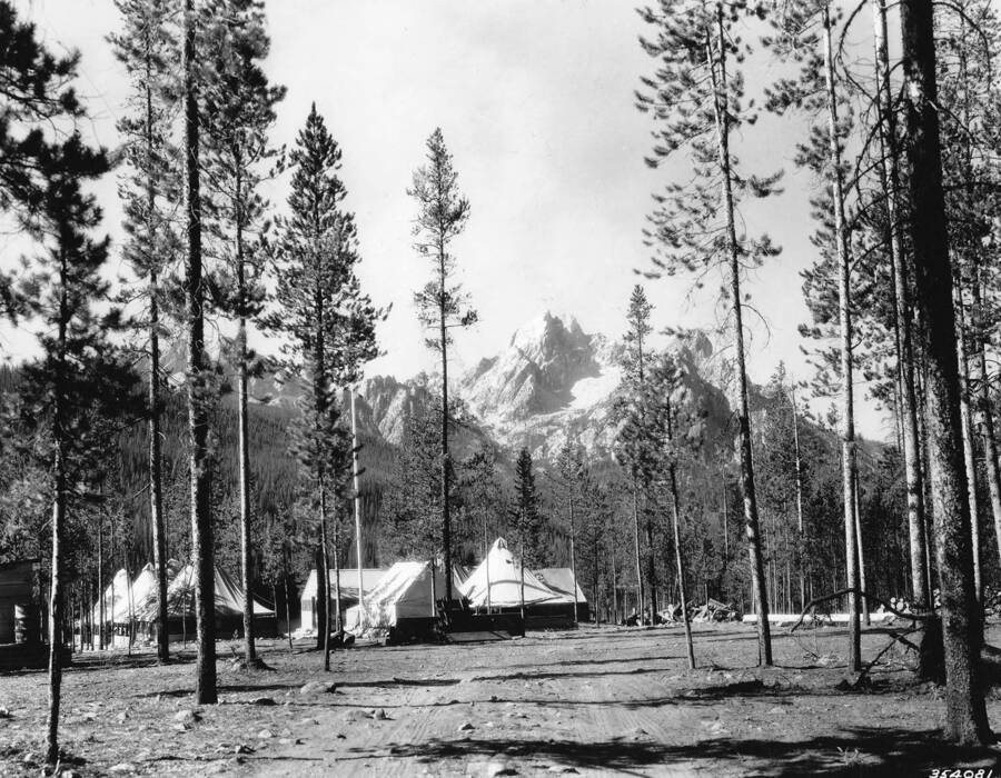 View of Stanley Lake spike camp in the Sawtooth National Forest and the Sawtooth Mountains in the background, Idaho. Writing above the photo reads: 'Operation and Information, Camps, Idaho, Sawtooth National Forest. Stanley Lake Spike Camp. Taken by W.H. Shaffer 1937.' Writing below photo reads: 'U.S. Department of Agriculture.'
