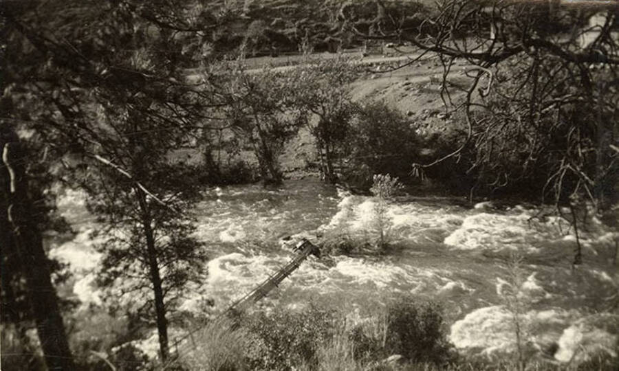 Photo of a river running rapidly, with a downed narrow construction leading from the bank into the middle of the river.