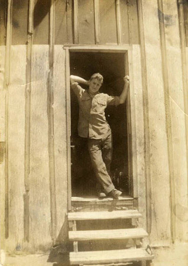 Photo of a CCC man leaning in the doorway of a barrack.