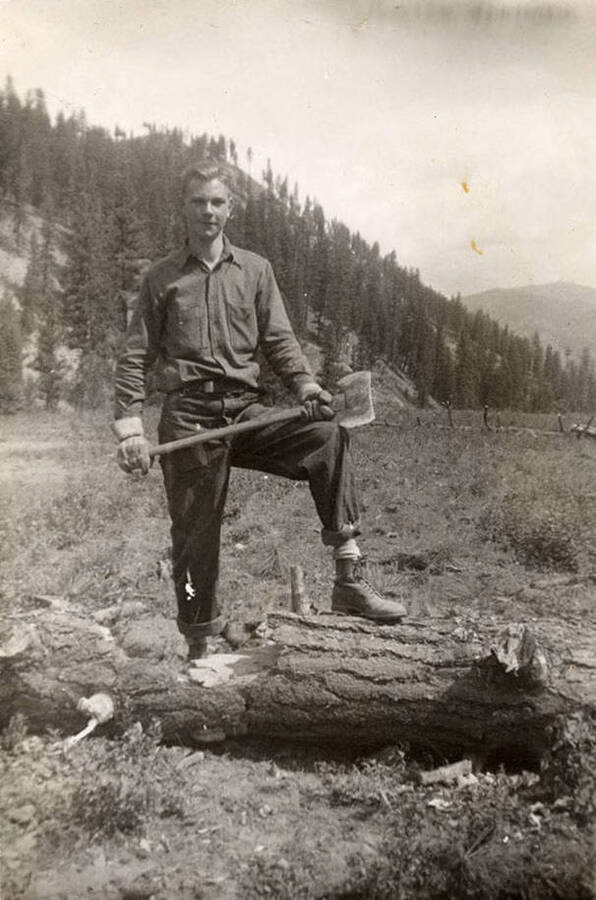 Mike McKinney posing in a field with an axe in his hand and his foot on a log. Writing on the album page reads: 'Vincent 'Mike' McKinney' Writing under the photo reads: 'Me'.