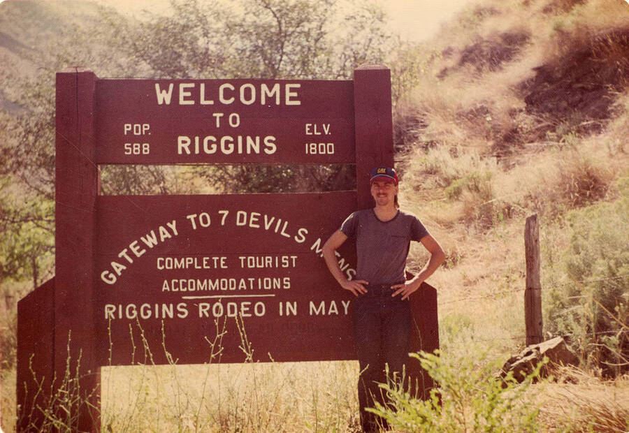 Town sign for Riggins. Sign reads: 'Welcome to Riggins Pop. 588 Elv. 1800 Gateway to 7 Devils M[T]NS Complete Tourist Accommodations Riggins Rodeo in May'.
