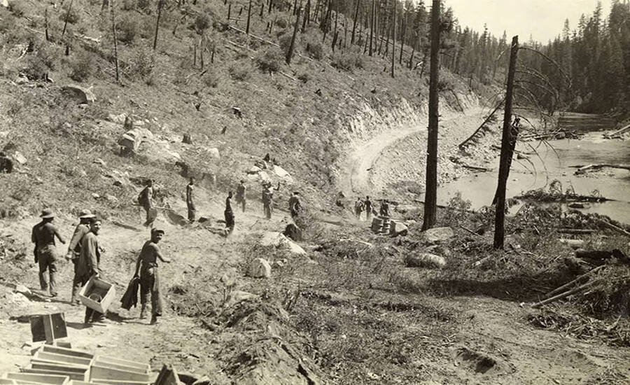 A CCC work crew walking back to camp from road work. Writing below the photo reads: 'Knocking off'.