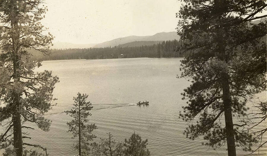 Landscape view of lake, and three figures sitting in a motorboat. Writing below the photo reads: 'Warm Lake Idaho.'
