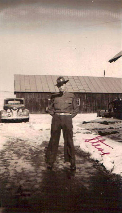Photo of a CCC enrollee standing in a snowy CCC camp with a building and truck in the background. Writing on the photo reads: 'Steve'.