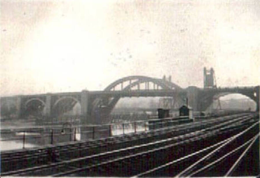 Photo of a bridge over a river with railroad tracks in the foreground.