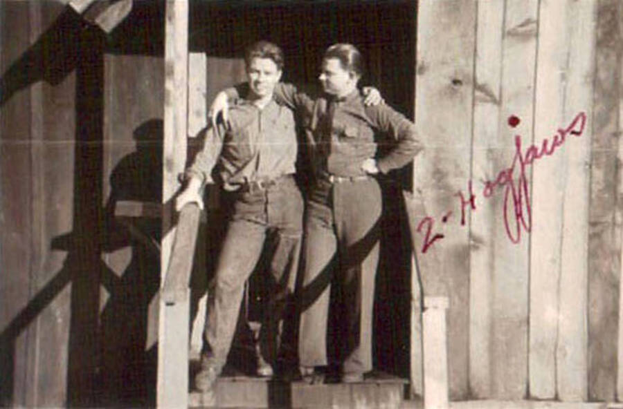 Two CCC men standing on the porch of a CCC building. Writing on the photo reads: '2-Hogjaws' in red ink.