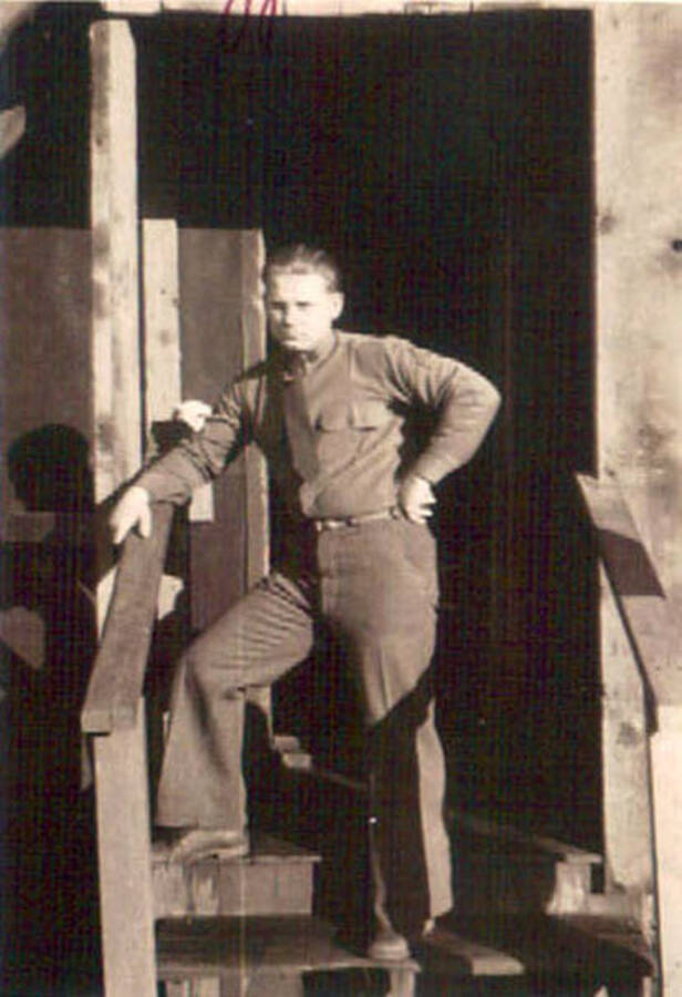 Portrait of a CCC man standing on the porch of a CCC barrack. Writing to the left of the photo reads: 'Brandy'. Writing above the photo reads: 'Hogjaw'.