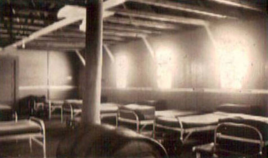 Photo of the interior of a barracks at the CCC camp in Moscow, Idaho.  There are rows of beds and a wood stove. Label on the album page reads: 'CCC Camp 1938-1939 Idaho'.