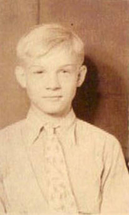 School photo of a young boy. Writing under the photo reads: '1938-39' Label on the album page reads: 'CCC Camp 1938-1939 Idaho'.