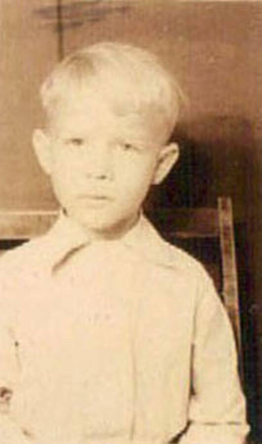 School photo of a young boy. Writing under the photo reads: '1938-39' Label on the album page reads: 'CCC Camp 1938-1939 Idaho'.