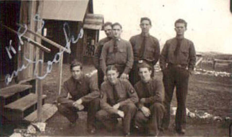 A group of CCC men posing in front of a CCC camp barrack. Writing on the photo reads: 'KP's and cooks' Label on the album page reads: 'CCC Camp 1938-1939 Idaho'.