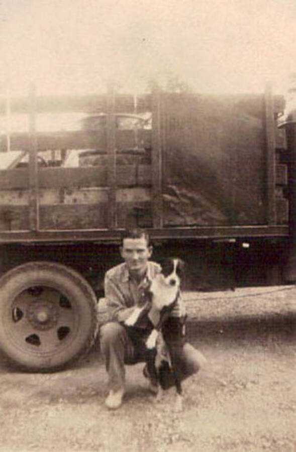 A CCC man kneels holding a dog next to a loaded truck.