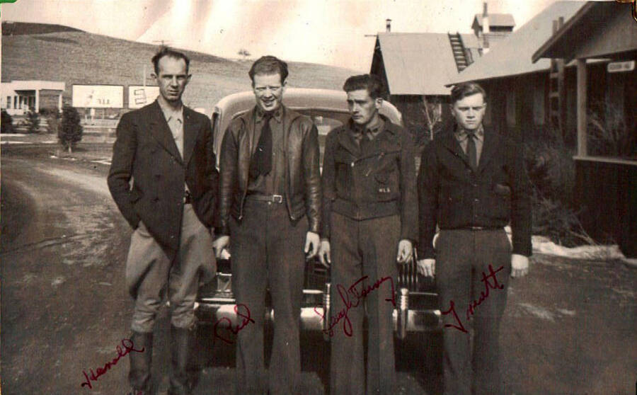 A group of four CCC men pose in front of a car in the road in front of a building at the Moscow, ID CCC Camp. Writing below the photos reads: 'The boys that I went to Walla Walla Wash. with'. Writing on the photo is the name of each man. Writing on the album page  that includes a duplicate photo reads: 'Lewiston, Idaho 1938 CCC Camp'. Writing under the duplicate photo reads: 'camp'.