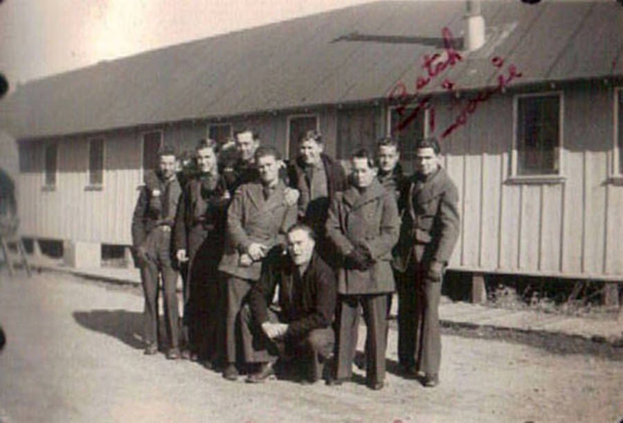 Group of CCC men posing for a photo standing next to a barrack. Writing on the photo reads: 'Batch + Louie' and refers to the two men standing furthest to the right of the photo. Writing under the photo reads: 'Leweston Idaho'.