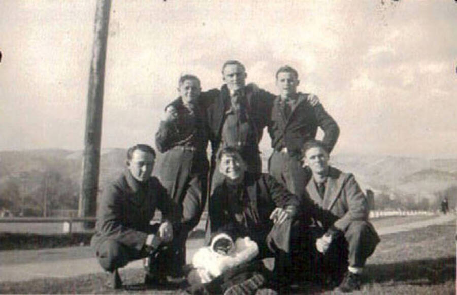 A group of CCC men posing for a photo. On the ground in front of a men is what appears to be some sort of animal in a Santa Claus costume. Writing under the photo reads: 'Lewiston Idaho'.