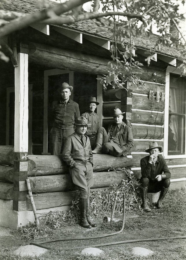 Five uniformed men stand posed for a photo in front of a building.