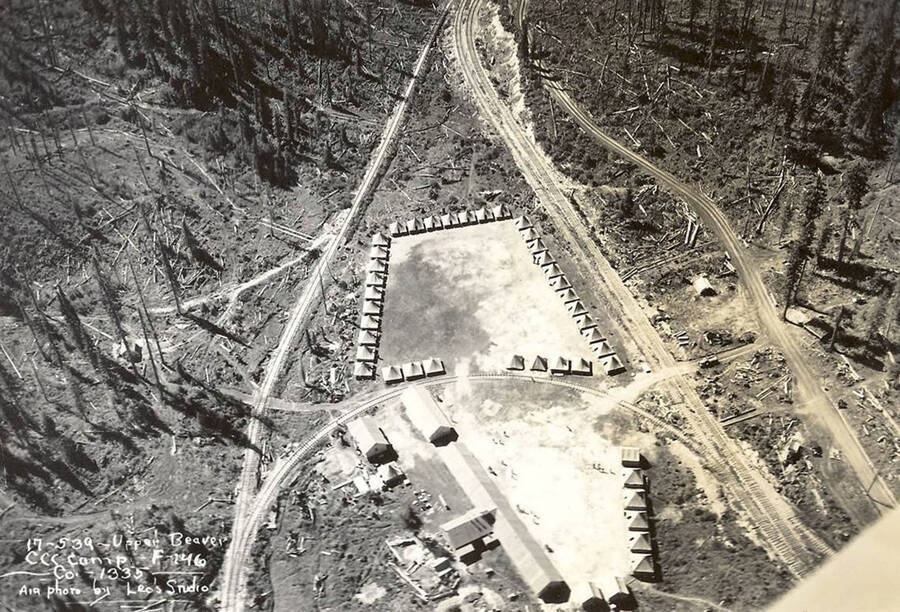 Aerial view of Upper Beaver CCC Camp. Several CCC buildings and tent barracks sit inbetween several roads and railroad tracks. Writing on the photo reads: '17-539- Upper Beaver CCC Camp F-146 Co. 1335 Air photo by Leo's Studio'.