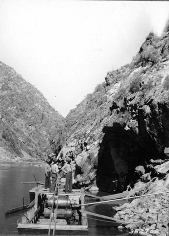 Photo of three CCC men on a boat on the Salmon River. Below the men is an air compressor used for drilling rock from the cliffs on the sides of the river.