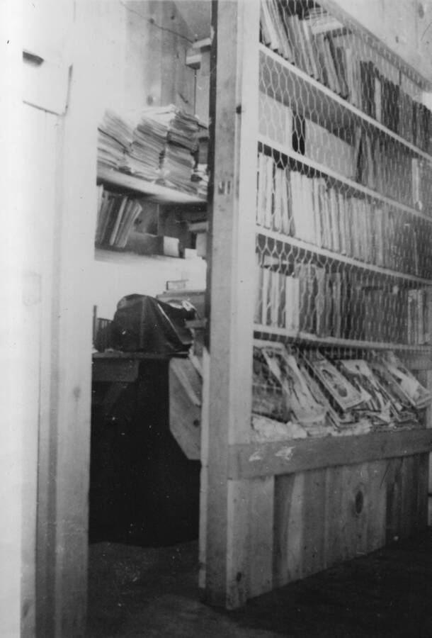 Books and Magazines line the shelves in the CCC Camp's education building to form the Camp 'Library'. Writing beneath the photo reads: '1850.0023. Camp Library, S-223, McCall, 1935'.