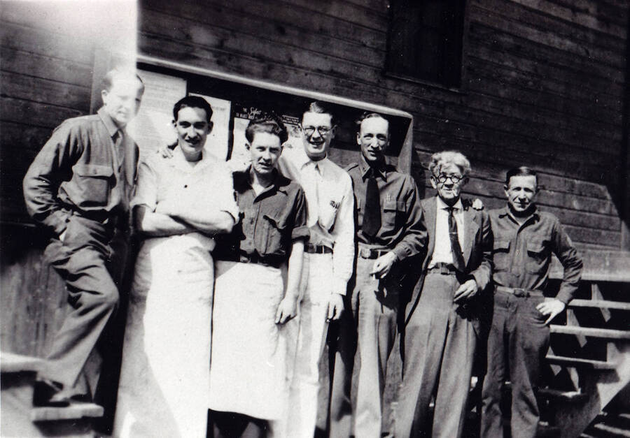 Group of CCC staff posed at Camp Kalispell Bay, F-142 they are part of Company 1994 stationed at Priest Lake, Idaho. This photo was taken in summer. The men are listed left to right as: Burgendorf, B. Yaryan, Fred Blood, E.B. Ball, Capt. Brown, Pop MacMiller, and Oscar Linton.