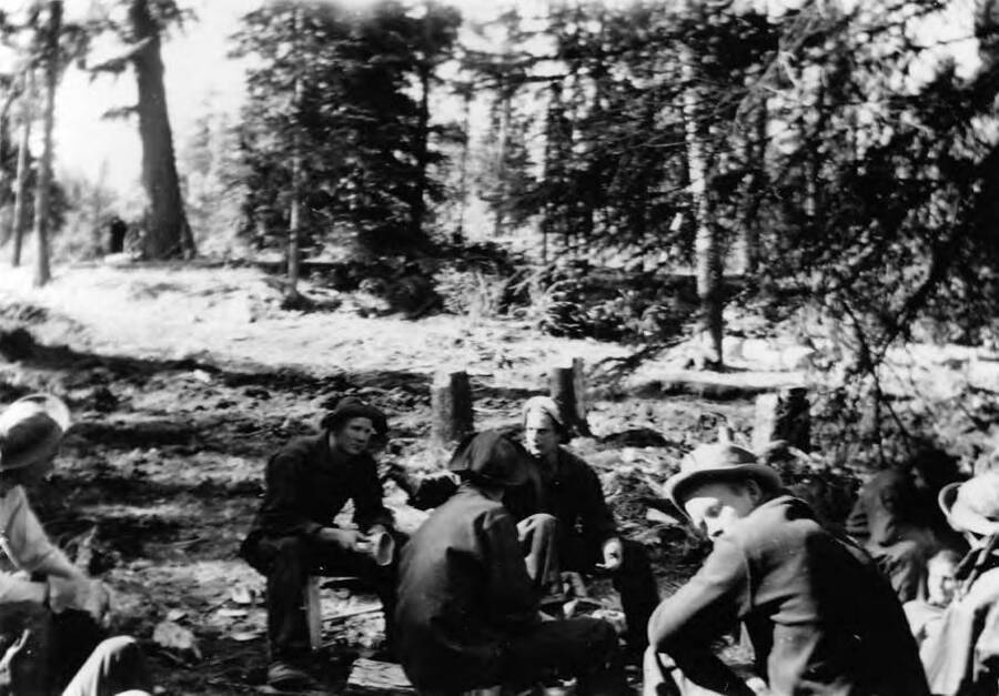 A group of men eat lunch in the forest near the Smiths Ferry camp. Writing beneath the photo reads: 'Photo No. 1850.0084. ''We eat!' eating lunch in the woods' C-1997 (?)'