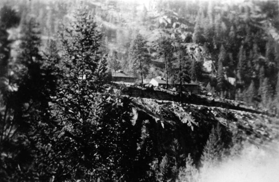 Camp French Creek can be seen among the trees of the Payette National Forest, from the bottom of a rock ridge. Writing beneath the photo reads: 'Photo No. 1850.0099. Camp French Creek, F-108'