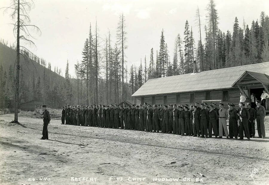 Uniformed CCC men standing at attention during retreat at Hudlow Creek Camp. Writing on the photo reads: 'Retreat F-113 Camp Hudlow Creek'.