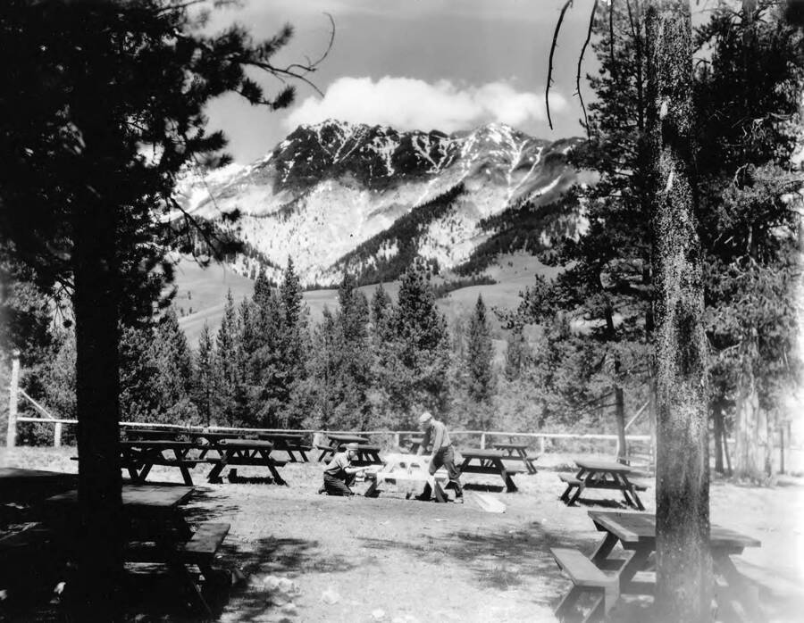 CCC men constructing camp tables at Camp Benedict, Sawtooth National Forest, Idaho. Sawtooth Mountains loom in the background.