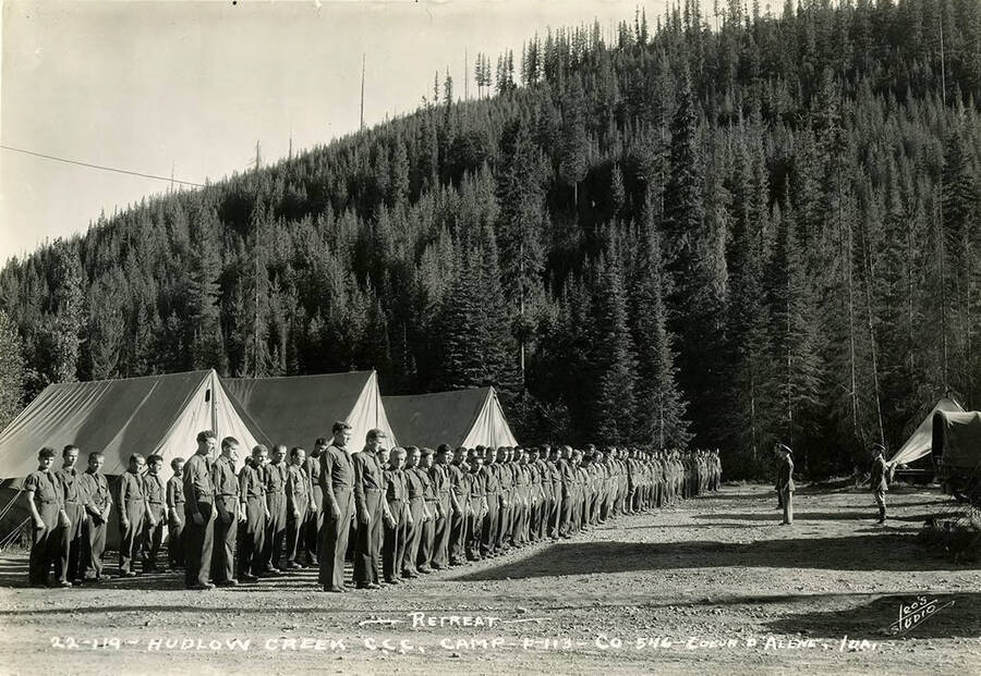 Uniformed CCC men standing at attention during retreat at Hudlow Creek Camp. Writing on the photo reads: 'Retreat Hudlow Creek CCC Camp F-113 Company 546 Coeur d'Alene, Idaho Leo's Studio'.