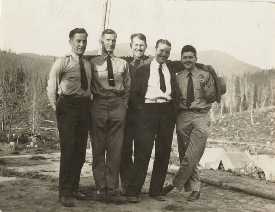 Personnel of Elk Basin Camp. The men, who are all wearing ties, are standing with their arms around each other. Names read as subjects appear, left to right: Penalta, B.B, Capt.; Gallagher, Hiram, Dr.; Field, E.W, E.A.; Matthews, H.E., Camp Sgt; Mansfield, W.C., Lt.