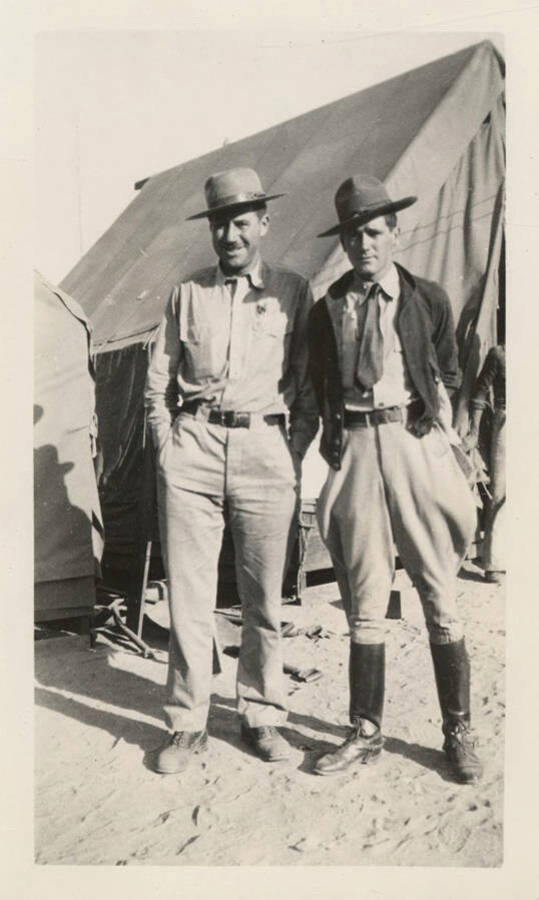 Lieutenant E. W. Field and Lieutenant W.C. Mansfield stand in uniform outside a tent in a CCC camp.