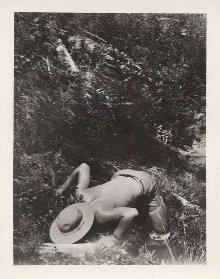 A man identified as Mr. Field bends down to drink water from a stream. The back of the photographs reads: 'Mr. Field-in a most ungentlemanly position!'