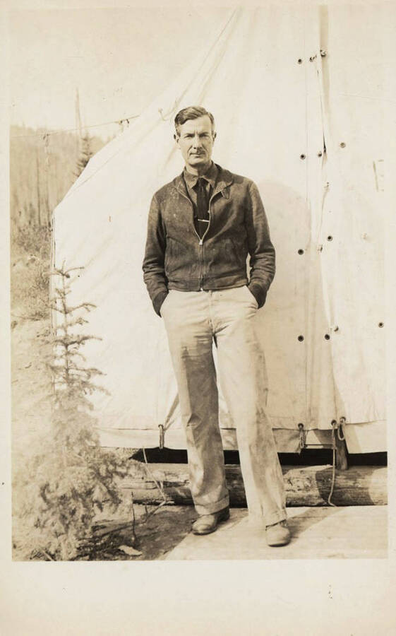 A postcard showing one of the camp personnel from the Elk Basin Camp. The man can be seen standing in front of a tent. Names read as subjects appear: Gallagher, Hiram, Dr.