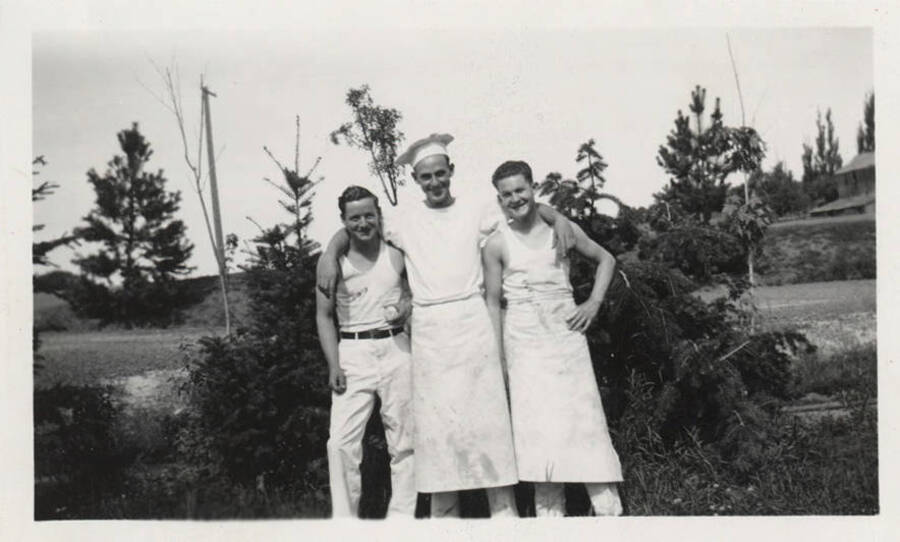 Three men dressed as the Camp cook staff pose for a group photo.