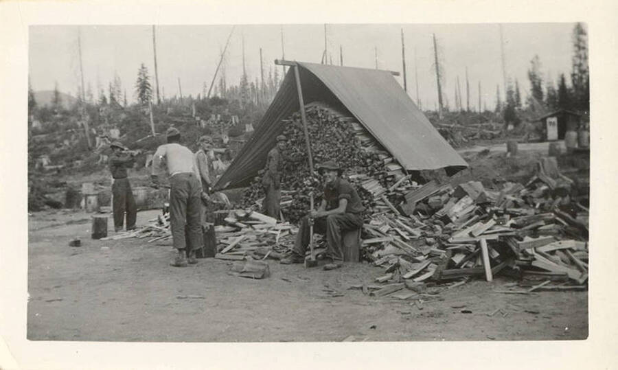 Enrollees splitting wood to work off their excess fines beyond their paychecks. The back of the photograph reads: 'Saturday morning working out their fines!'