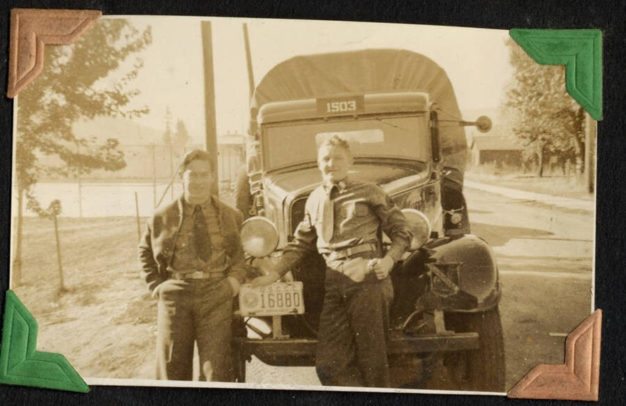 Two men in military uniform posing next to CCC covered truck. SCS-1, C-1503. From the Paul Saft photographic album, SCS-1, C-1503, 1938-39, depicting camp life, taken mostly in the Moscow, Lewiston, Robinson Lake areas.