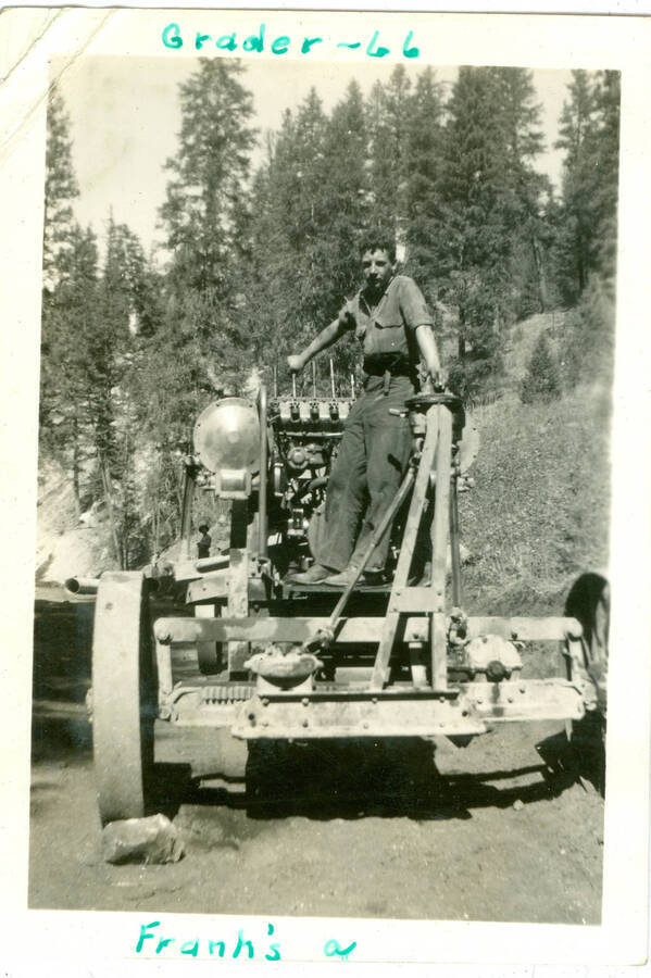 Picture of man on grading equipment. Handwritten caption:  'Grader-66' 'Franh's a' Trucks and logs in the background; pipe in the foreground.  This is likely to be located at near Camp Creek, South Fork of the Salmon River, which built Krassel Ranger Station.
