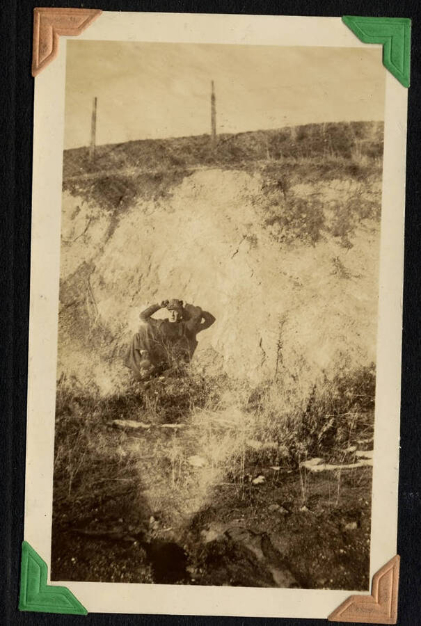 Man resting in deep gully above fenced field. SCS-01, C1503. From the Paul Saft photographic album, SCS-1, C-1503, 1938-39, depicting camp life, taken mostly in the Moscow, Lewiston, Robinson Lake areas.