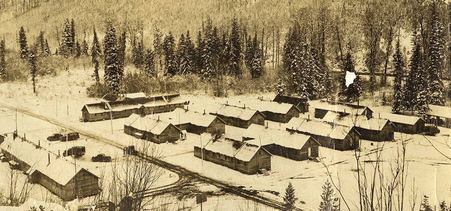 Overview of Big Creek 2 CCC Camp taken from the hillside above camp. Buildings are as follows: far left is the headquarters building which housed the supply room, recreation room, canteen, main office, and quarters for the non-coms. Long building in the back is the kitchen and mess hall. Middle row to the right of the u-shaped building is the barracks (8 in total) each sleeping 25 men. Originally there was a latrine between every other barrack but they were replaced by the two buildings on the end of each row of barracks (far right). in-between the two latrines is the Education building/library, this is where the educational advisor stayed. Writing on the photo reads: 'CCC Company 531 Camp Big Creek #2 F-132 Prichard, Idaho 1938'.