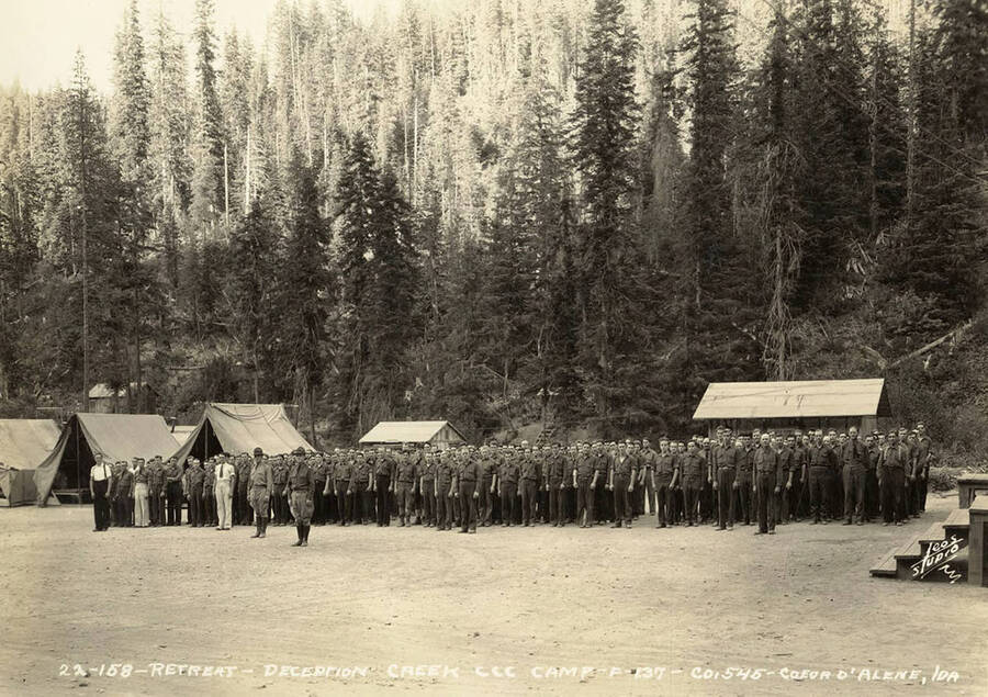 Uniformed CCC men standing at attention during retreat at Deception Creek CCC Camp. Writing on the photo reads: ' Retreat Deception Creek CCC Camp F-137 Company 545 Coeur d'Alene, Idaho Leo's Studio'.