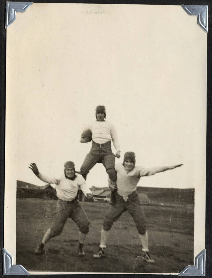 Three men in football gear, posed in a pyramid. SCS-1, C-1503. From the Paul Saft photographic album, SCS-1, C-1503, 1938-39, depicting camp life, taken mostly in the Moscow, Lewiston, Robinson Lake areas.