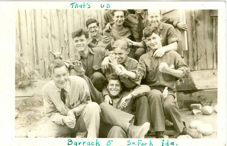 Informal group picture from photo album of nine enrollees and one military personnnel, Barrack 5, South Fork, Idaho. Handwritten in ink: 'That's us Barrack 5 S. Fork Ida.' This is likely to be located at Camp Creek, South Fork of the Salmon River, which built Krassel Ranger Station.