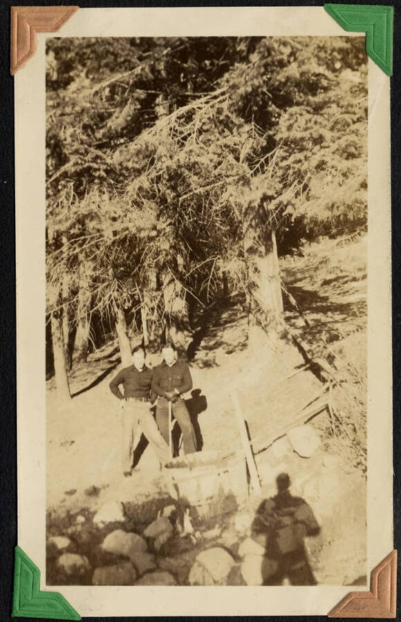 Two enrollees wearing dark shirts, one holding a tool handle, posed in front of round wooden trough. SCS-1, C-1503. From the Paul Saft photographic album, SCS-1, C-1503, 1938-39, depicting camp life, taken mostly in the Moscow, Lewiston, Robinson Lake areas.
