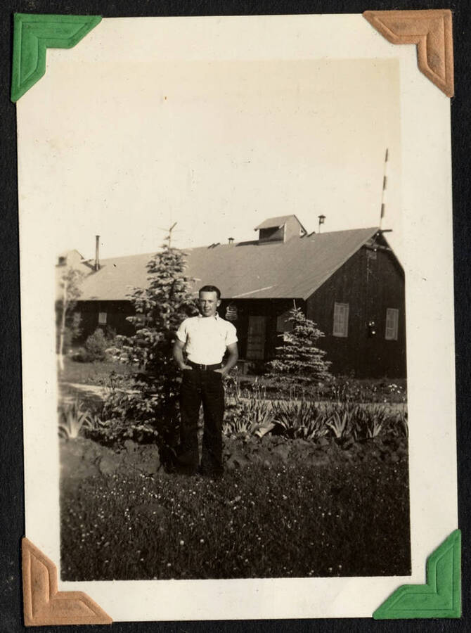 Picture of enrollee standing in front of a large building. From the Paul Saft photographic album, from SCS-1, C-1503, 1938-39, depicting camp life, taken mostly in the Moscow, Lewiston, Robinson Lake area, 1938-39.