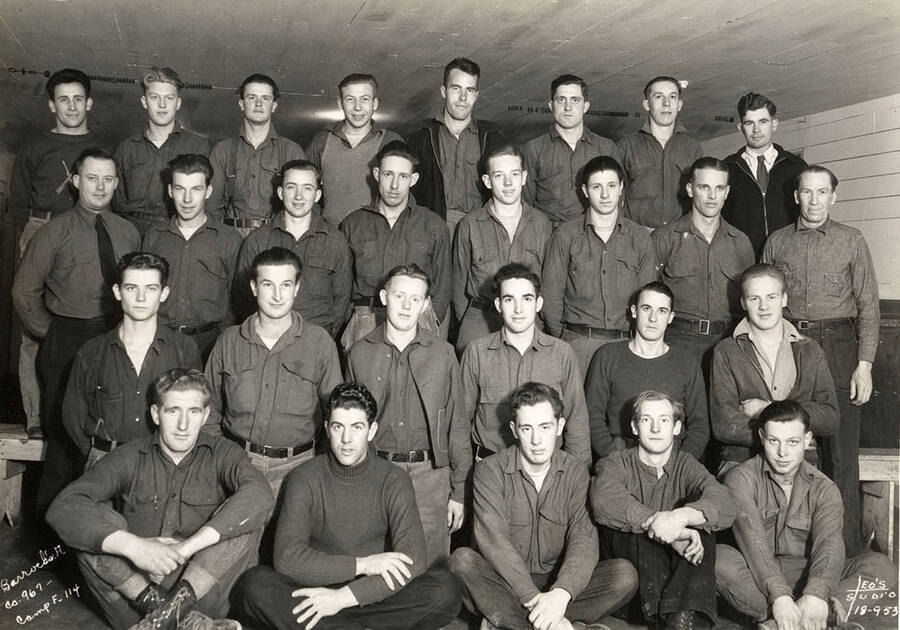 Group portrait of CCC men from Barracks A in the Cataldo CCC Camp. The man in the 3rd row back, third from left is Bernard Chambers'. Writing on the photo reads: 'Barracks A Company 967 Camp F-114 Leo's Studio'.