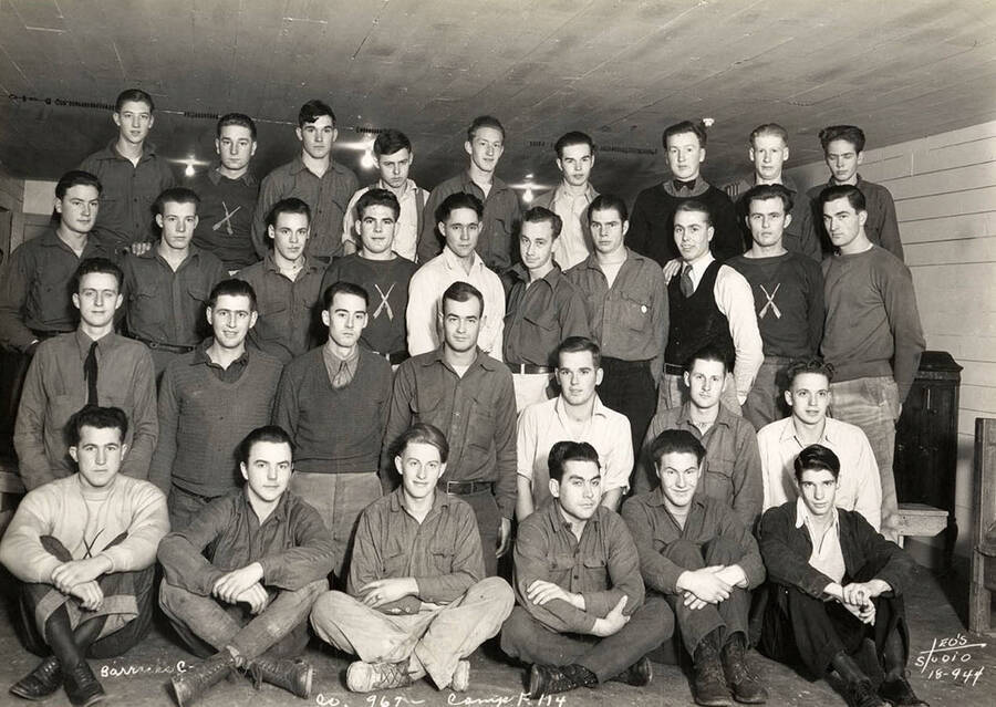 Group portrait of CCC men from Barracks C in the Cataldo CCC Camp. Writing on the photo reads: 'Barracks C Company 967 Camp F-114 Leo's Studio'.