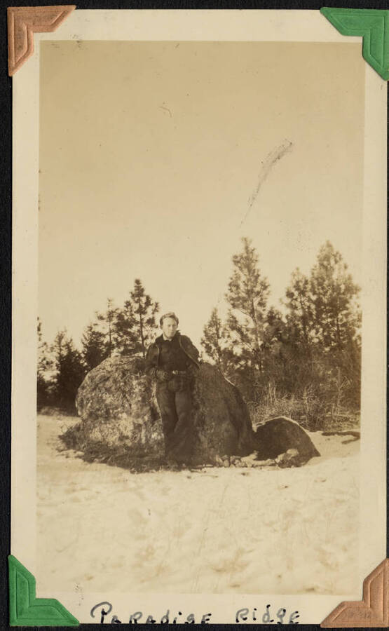 Man leaning against rock in snow, captioned 'Paradise Ridge,' SCS-1, C-1503. From the Paul Saft photographic album, SCS-1, C-1503, 1938-39, depicting camp life, taken mostly in the Moscow, Lewiston, Robinson Lake areas.